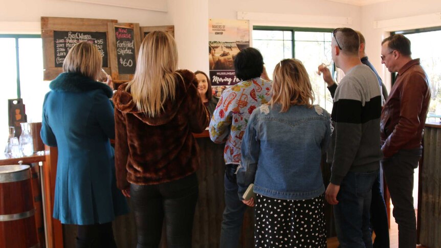 A group of people stand around a bar sampling wine.