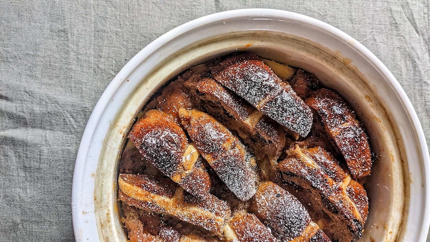 Chopped up hot cross buns in a white baking dish covered in white sugar.