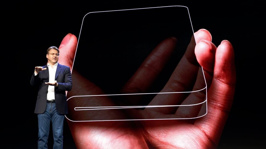 A man stands in front of a screen displaying the outline of a tablet that folds over on itself