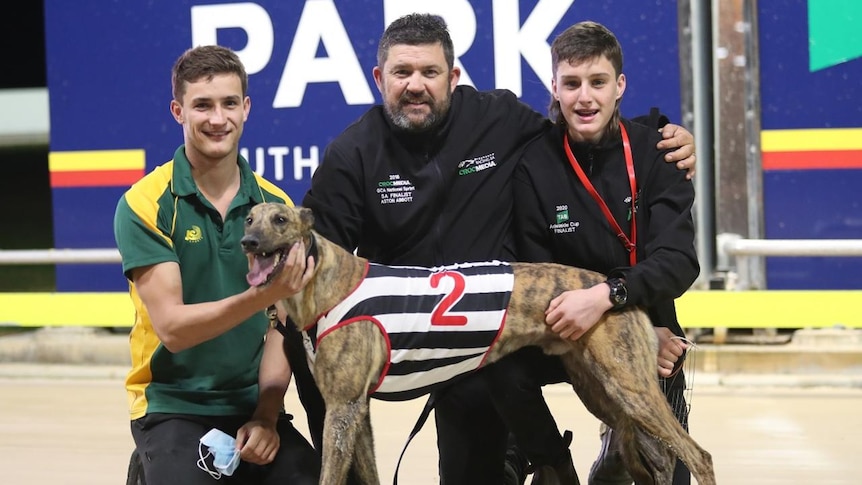Three people with a greyhound on a track.