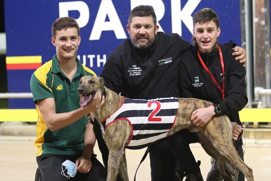 Three people with a greyhound on a track.