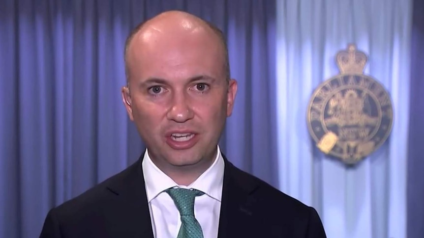 A bald man in a suit and tie looks at the camera from New South Wales Parliament