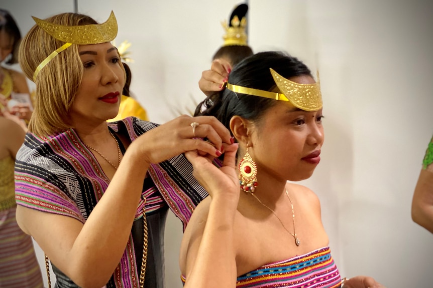 A woman in traditional costume helping another woman do her hair