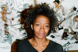 A portrait of an African American woman in her early 50s, standing in front of an artwork 