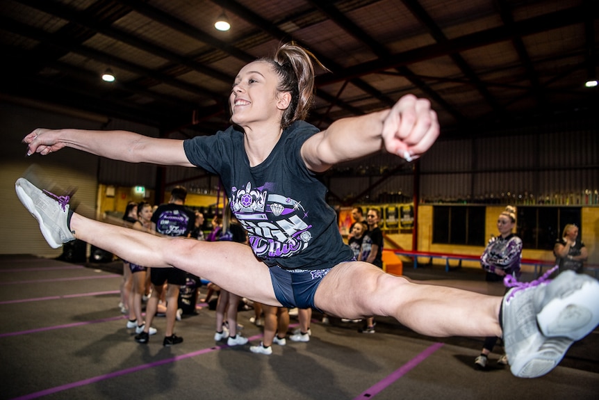 A teenage girl jumps in the air and does the splits.