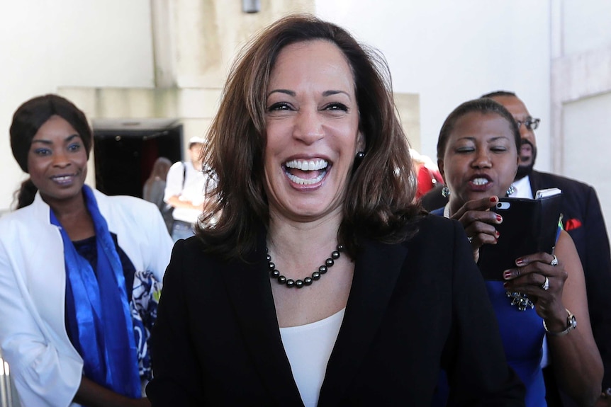 US senator Kamala Harris smiles widely as she walks ahead of three other people.