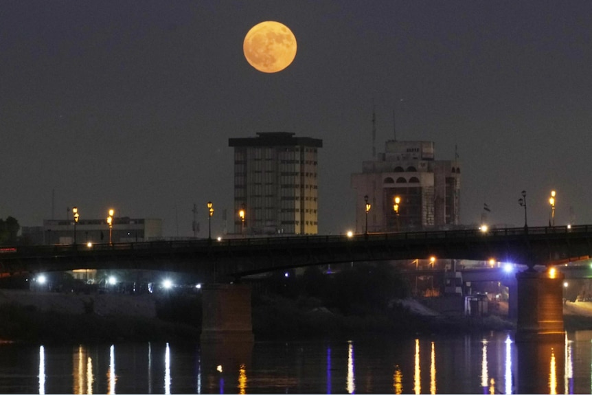 A yellow full moon rises above a city in the night sky 