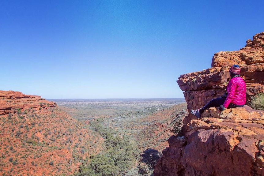 A person sits at the top of a rocky mountain range