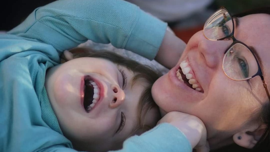 A mother laughs with her young son as they lay together.