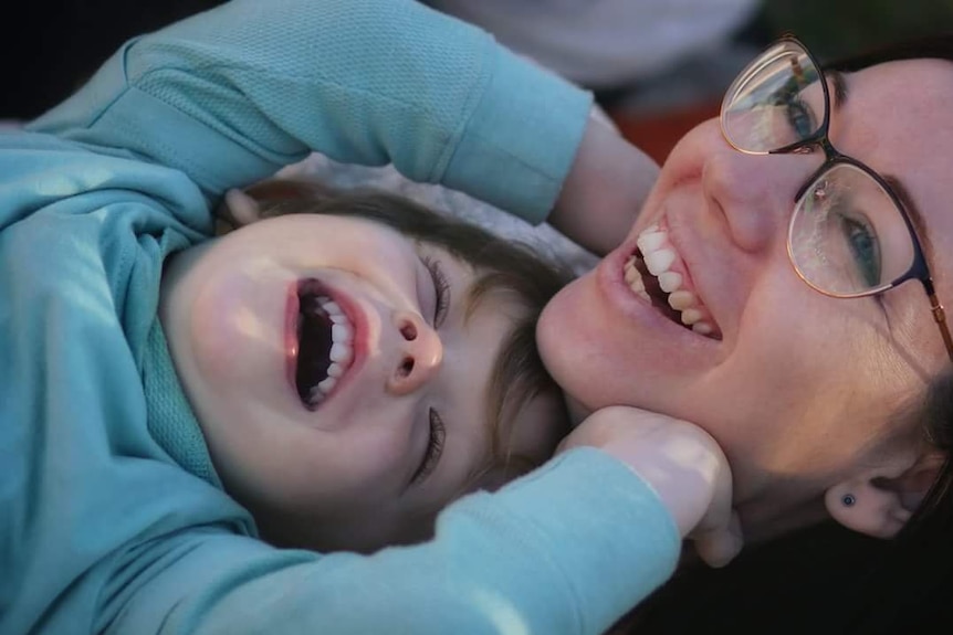 A mother laughs with her young son as they lay together.