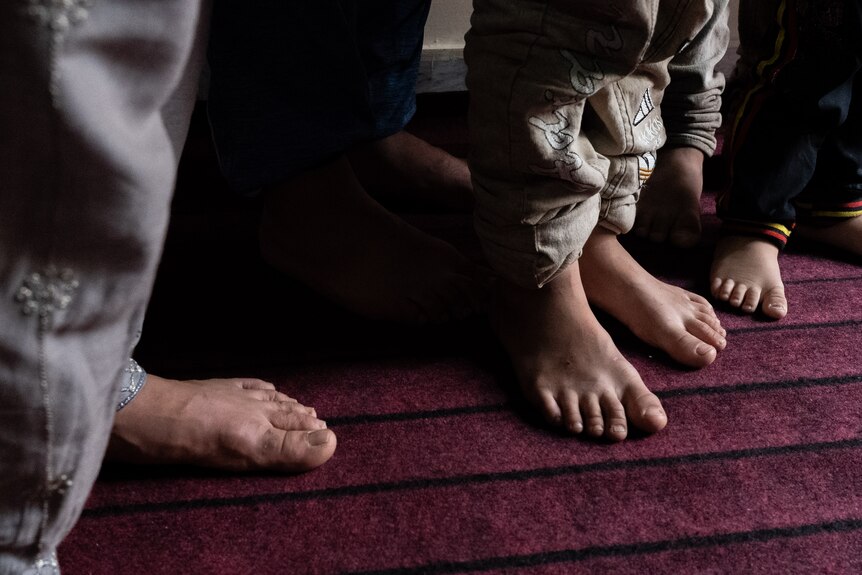 A shot of feet against the plum-coloured carpet. The feet belong to women and children 