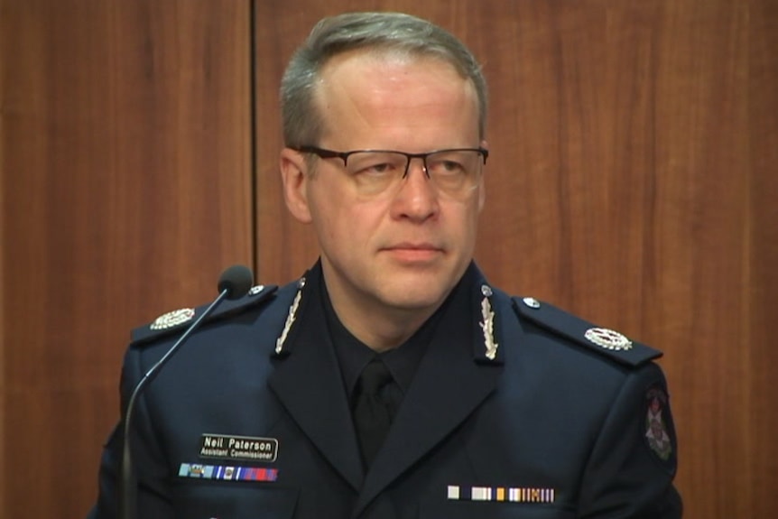 Victoria Police Assistant Commissioner Neil Paterson sits in police uniform in a witness box, in front of a microphone.