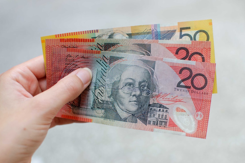 A woman holds a $50 note and two $20 notes for a story about superannuation.