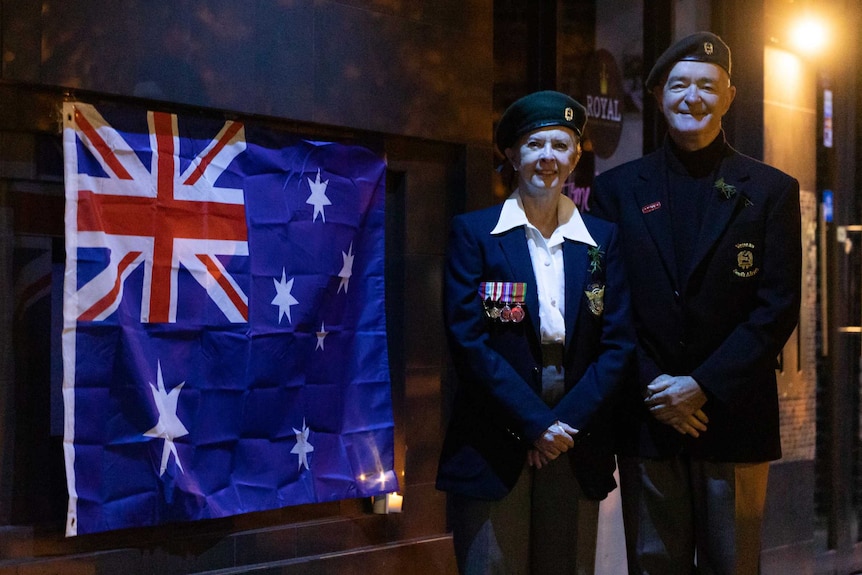 A man and woman in uniform pose next to an Australian flag.