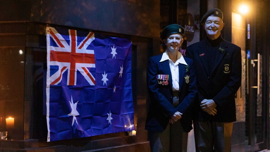 A man and woman in uniform pose next to an Australian flag.