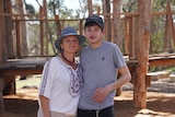 A mum and her son look at the camera with a wooden playground in the background.