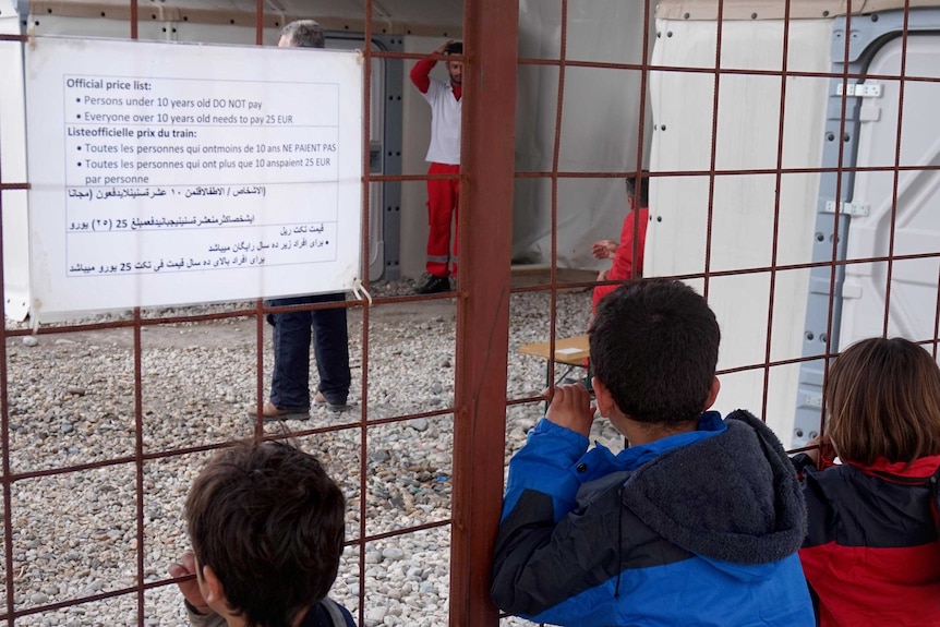 Iraqi children look through a fence below a sign detailing the price of the train to the Serbian border.