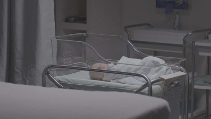 Baby wrapped in blanket in cradle in hospital room