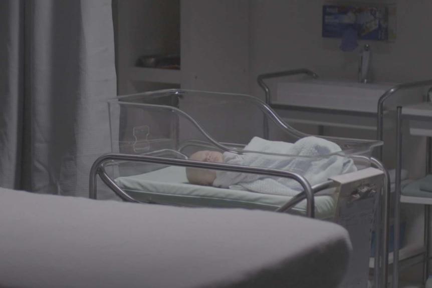 Baby wrapped in blanket in cradle in hospital room