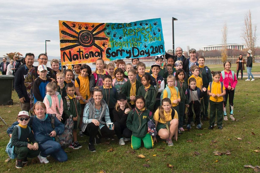 Young people pose for a photo, holding a banner that reads "respect and stand together, National Sorry Day."