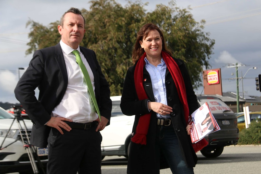 Mid shot of Mark McGowan and Tania Lawrence standing outside with a Hungry Jacks sign behind them.