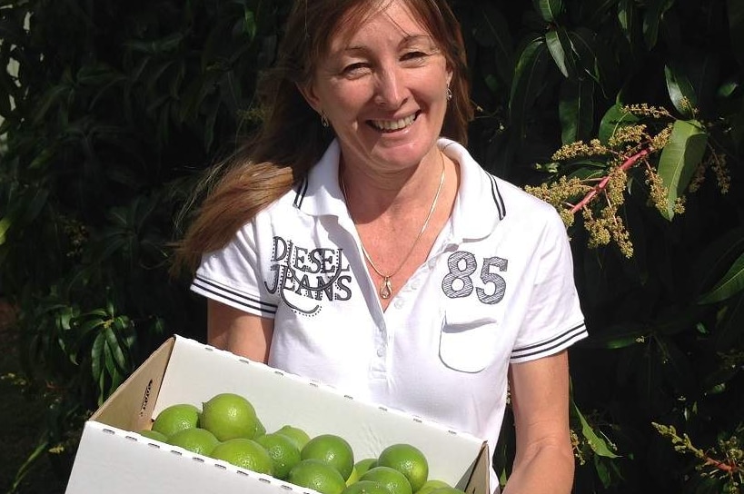 Karen Muccignat standing in front of a tree holding a box of limes