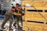 Soldiers push wooden boxes of cargo. 