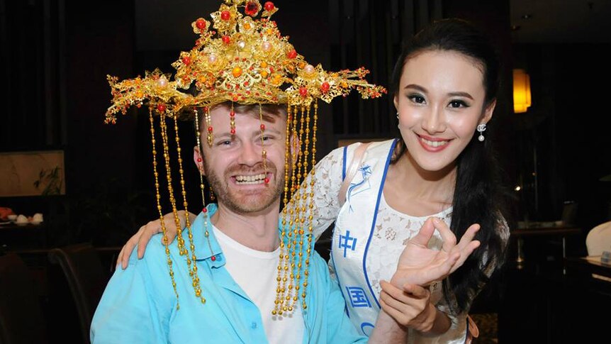 A man in traditional Chinese headwear poses with a female beauty pageant contestant.