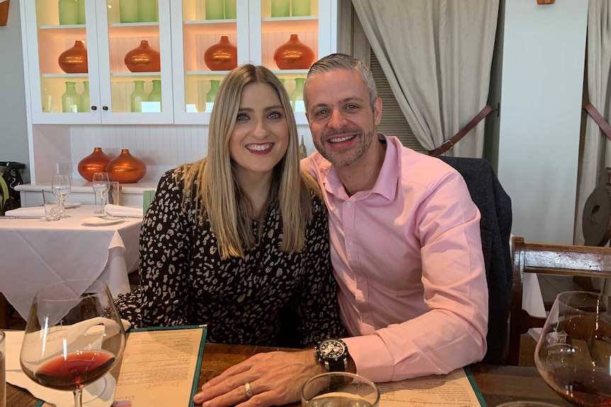 A man and woman look at the camera while sitting at a table in a restaurant.