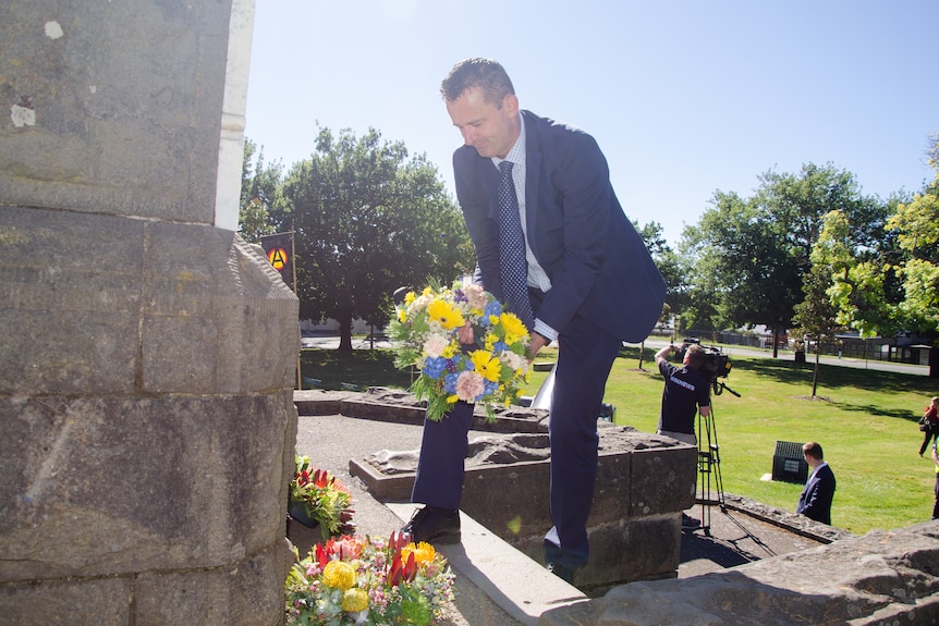 A man in a suit lays a wreath at the bottom of a large concrete monument.