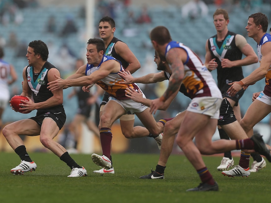 A Port Adelaide AFL player holds the ball and looks to change direction as he is chased by Brisbane players. 