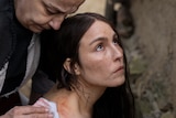 A woman with long dark hair, brown eyes and freckles looks up while an older woman looks over her shoulder