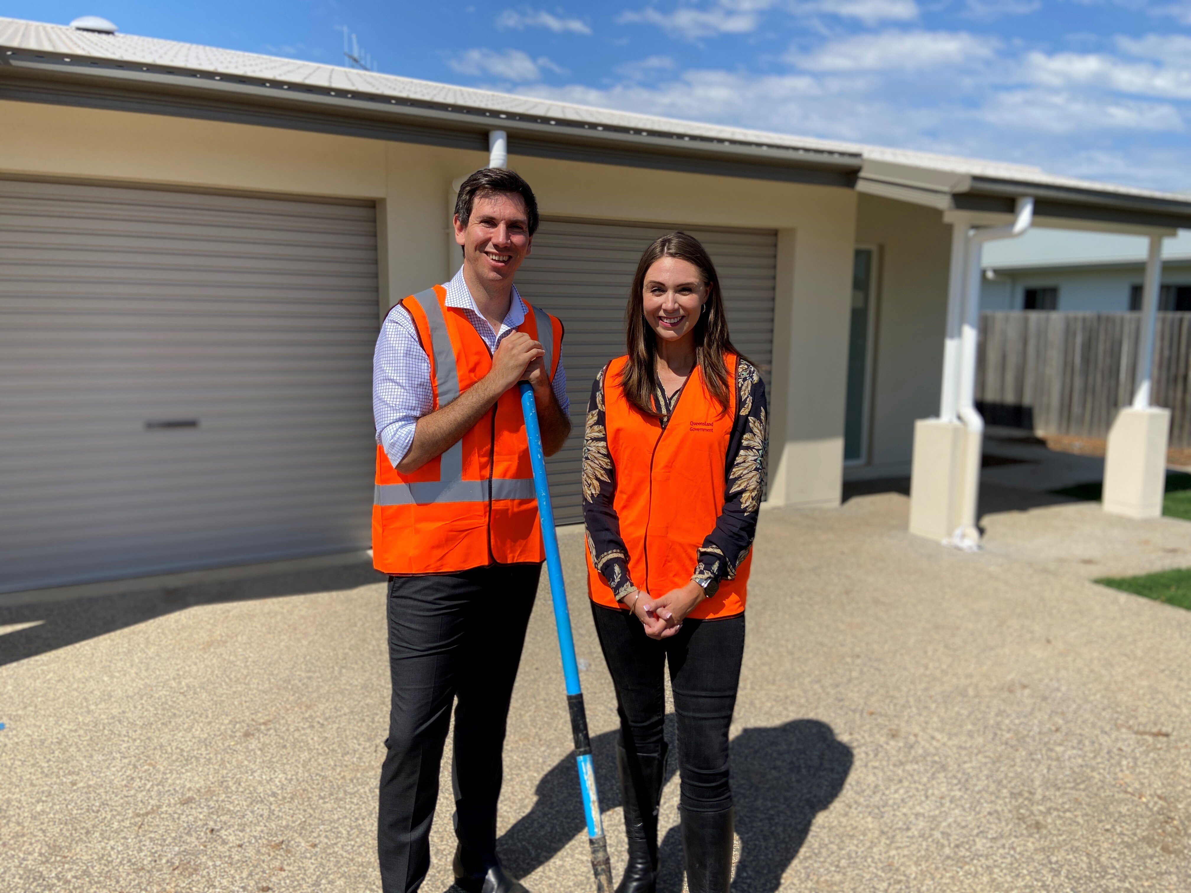 A smiling man and woman in high-vis standing in front of a new residential building.