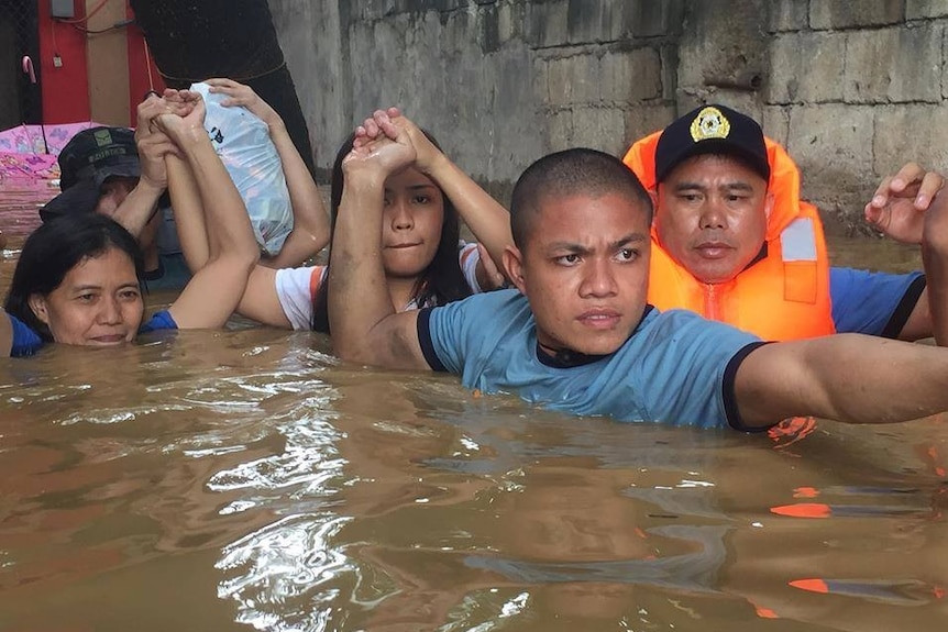 Three police officers help hold the hands and belongings of two women in brown floodwaters up to their necks