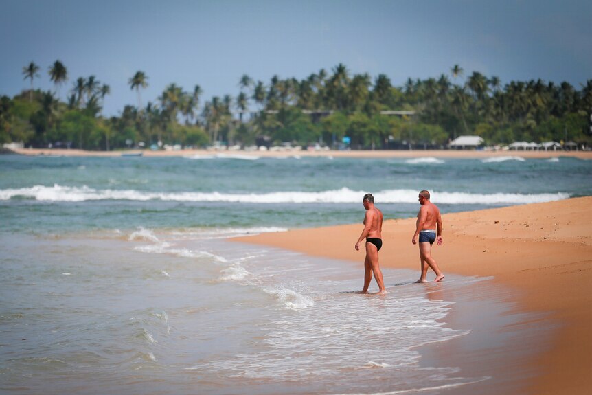 两名身穿紧身泳裤的男子在海滩上