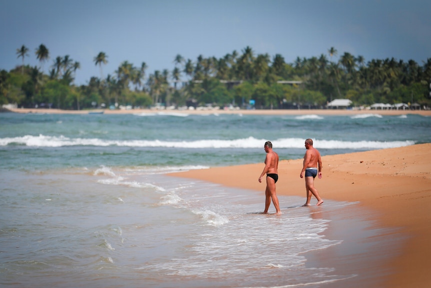 Two men in Speedos wandering along a tropical beach in Sri Lanka 