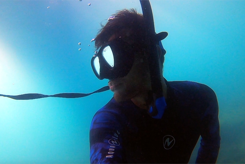 A scuba diver takes a photo of himself in a wetsuit with a mask