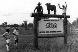 A 1983 'Victoria River research Station' sign with four employees beside and on it.
