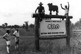 A 1983 'Victoria River research Station' sign with four employees beside and on it.