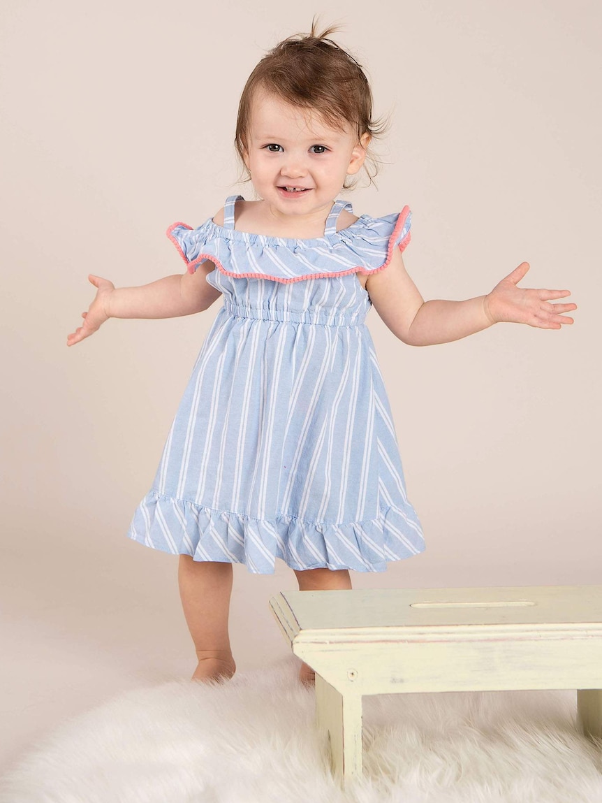 A little girl smiling and holding her arms open next to a baby piano