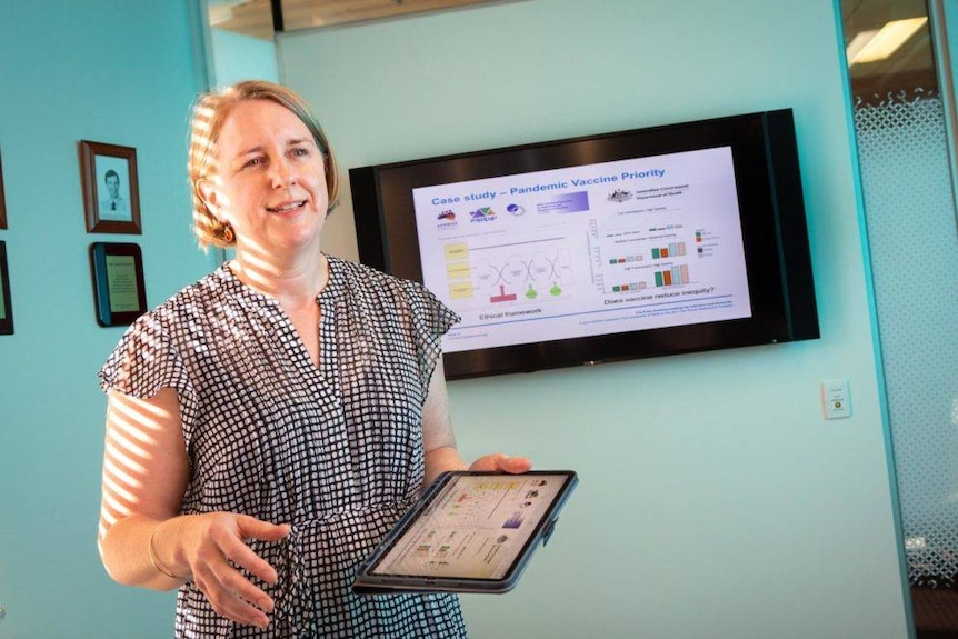 A woman with short blonde hair speaking with an ipad and sunlight streaming in.