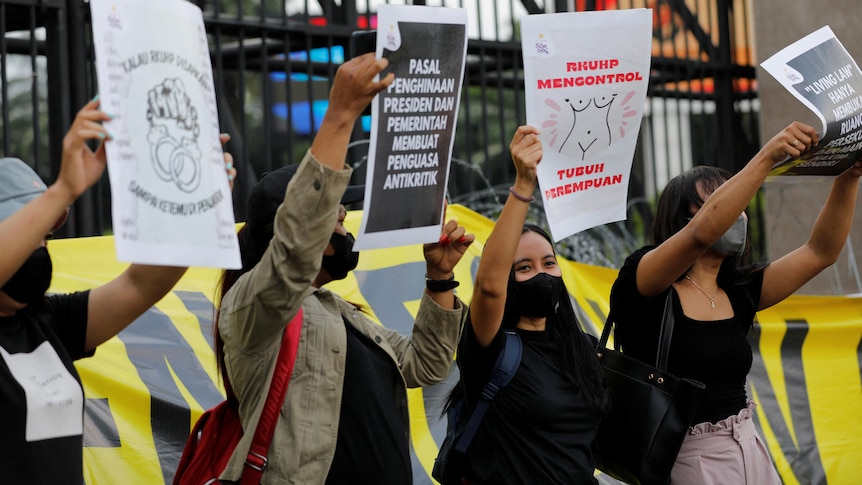 People hold up signs in Indonesian during a protest outside a gated building.