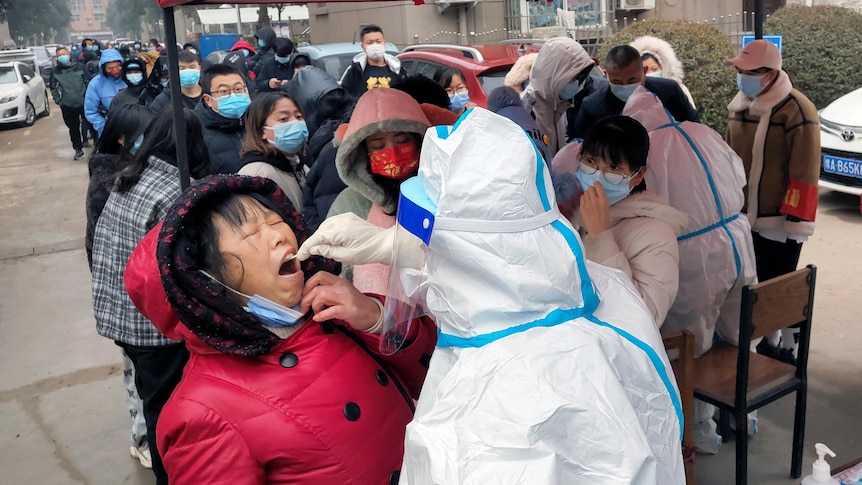 A woman closes her eyes as a person in full PPE uses a swab to collect material for testing from the woman's mouth.