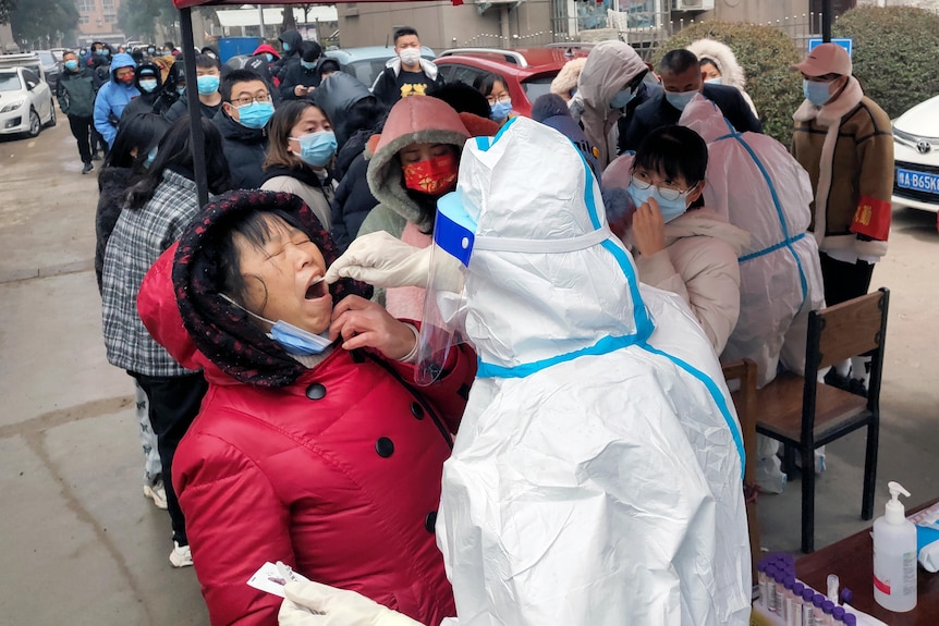 当一个拥有完整 PPE 的人使用棉签从该女性口中收集材料进行检查时，该女性闭上眼睛。