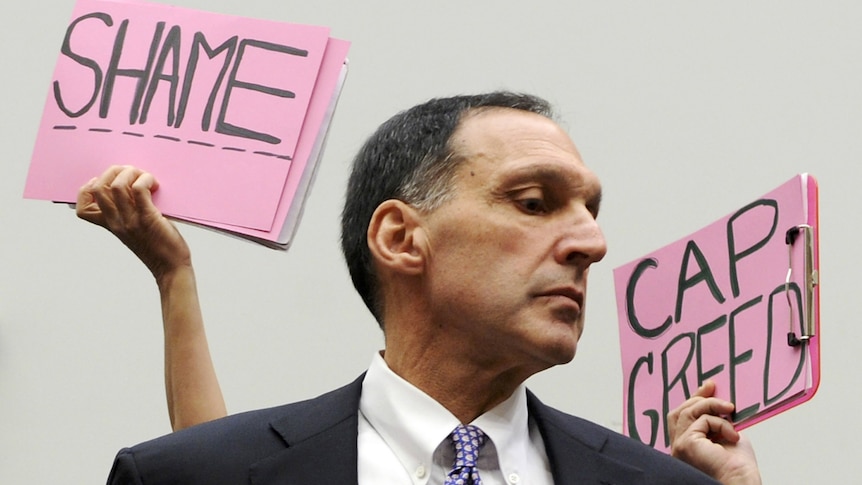 Protesters hold signs behind Richard Fuld, chairman and chief executive of Lehman Brothers Holdings.