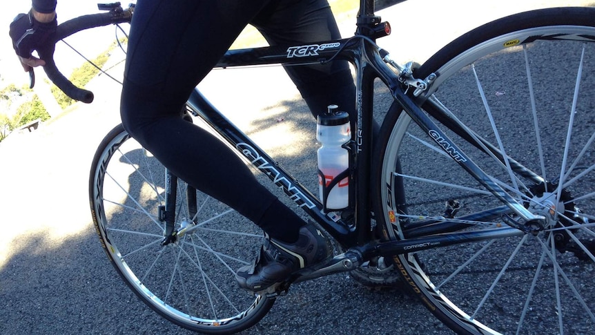 Cyclist on a bike, showing the cyclist's legs and two wheels of the bike.