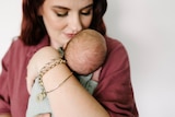 Mother holding a small baby on her shoulder.