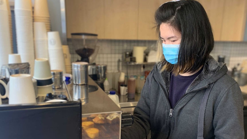 Barista Ticha Naksomyat steams milk for a coffee while wearing a mask at a cafe in Ultimo.