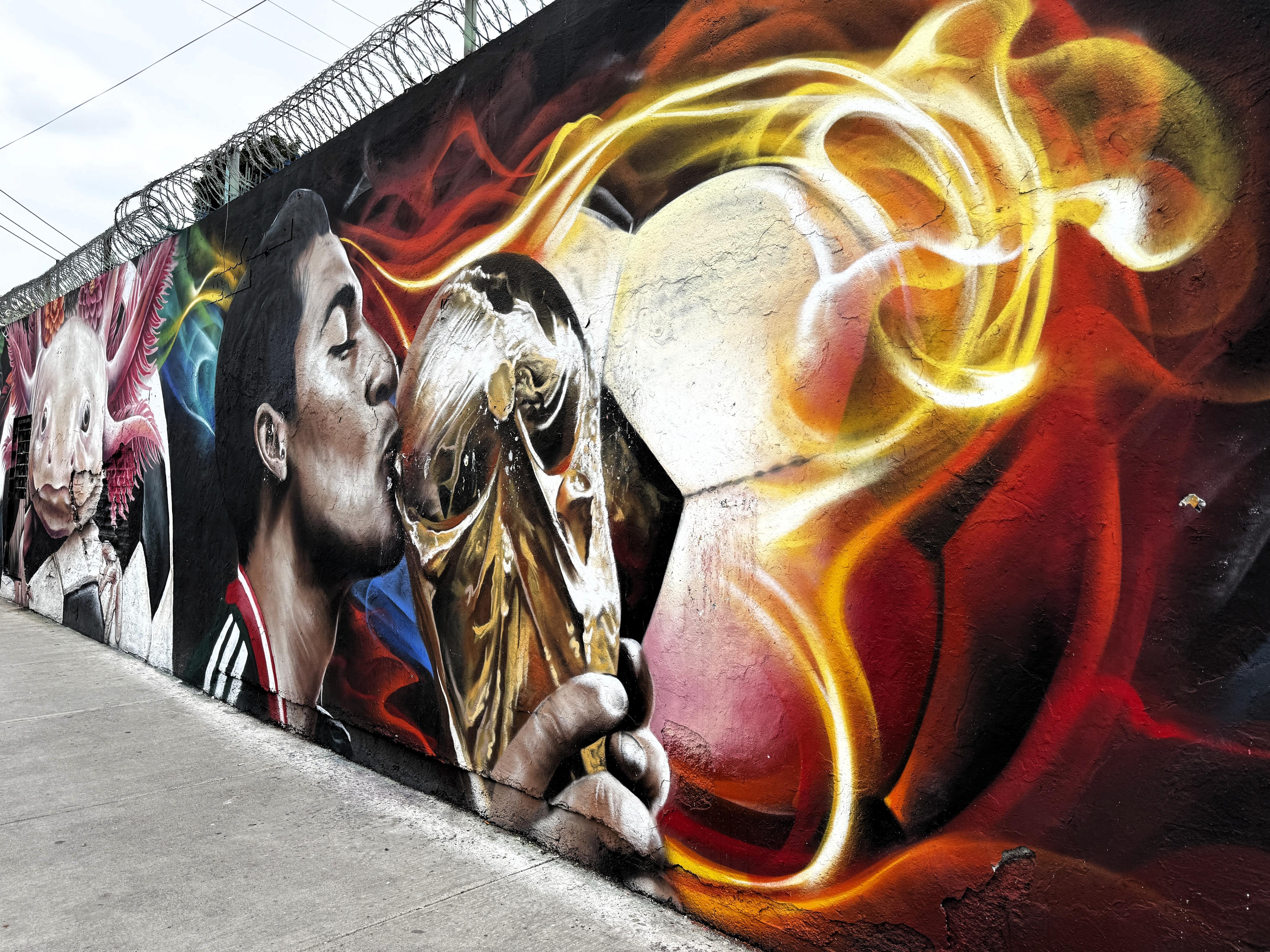 A wall mural of a male footballer kissing the World Cup trophy and a soccer ball engulfed in flames