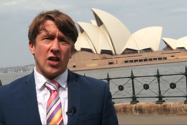 A man in a blue suit standing in Sydney Harbour with the Opera House in the background.